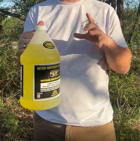 A person holding the product bottle at chest height outdoors, framed below the chin so the face is not in the shot. Caption: Scale example 2. Product shown being held without showing a full face.
